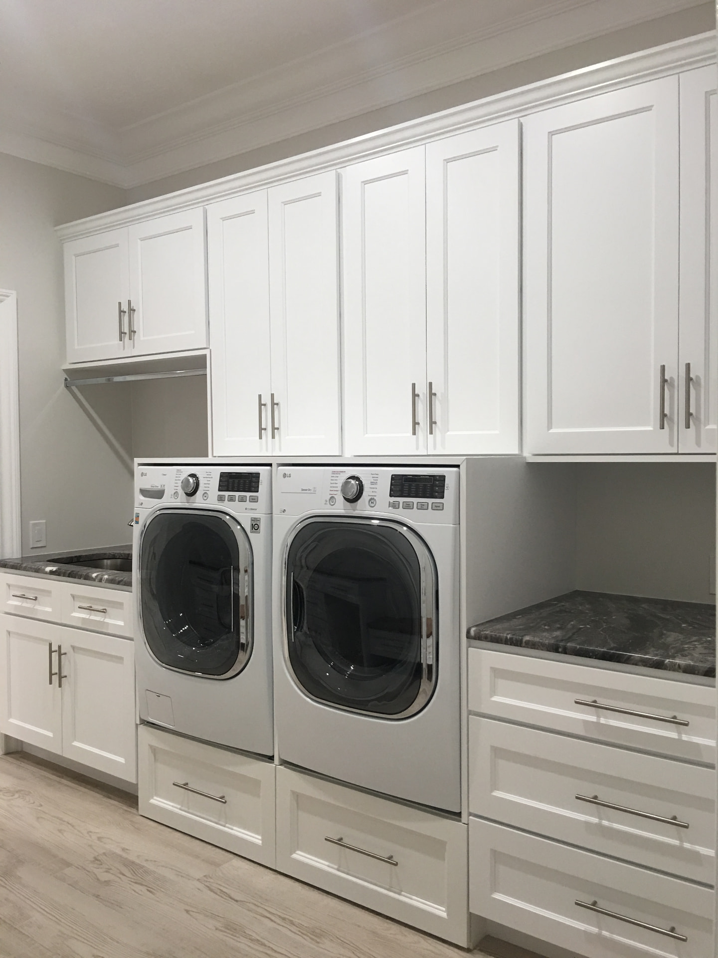 White shaker laundry cabinetry surrounding a raised front-loading washer and dryer
