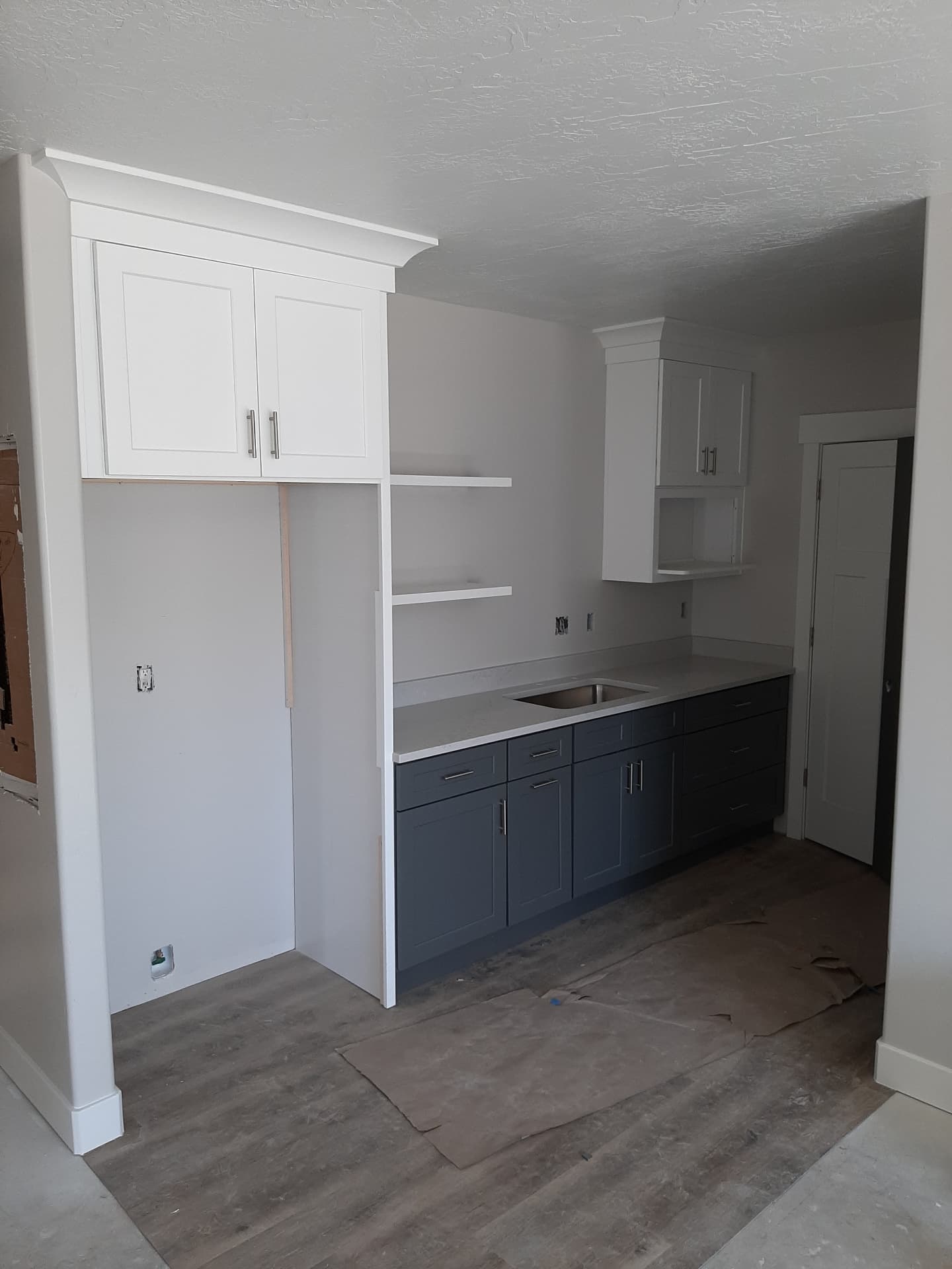 Two-tone kitchenette with navy base cabinets, quartz counter, white uppers and floating shelves