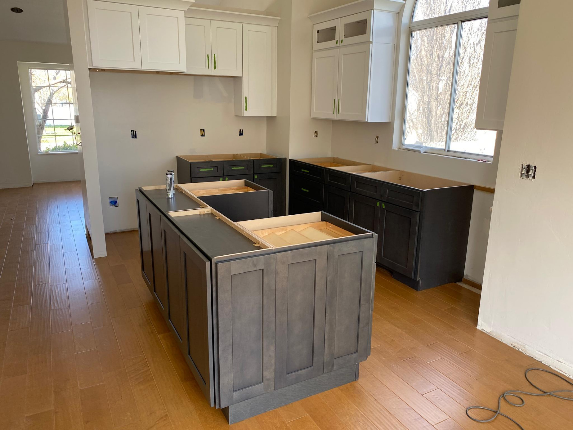 White shaker upper cabinets above charcoal base cabinets and a grey island during installation