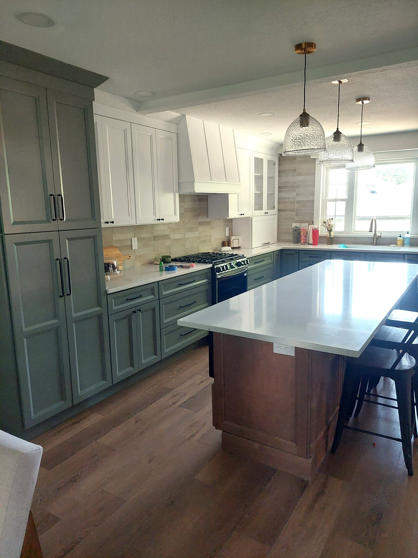 Muted green-grey kitchen cabinetry with white upper cabinets and a contrasting stained island
